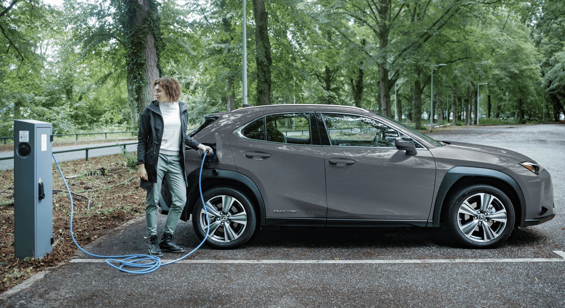 Vrouw laadt haar grijze elektrische auto op aan een openbare laadpaal in het park