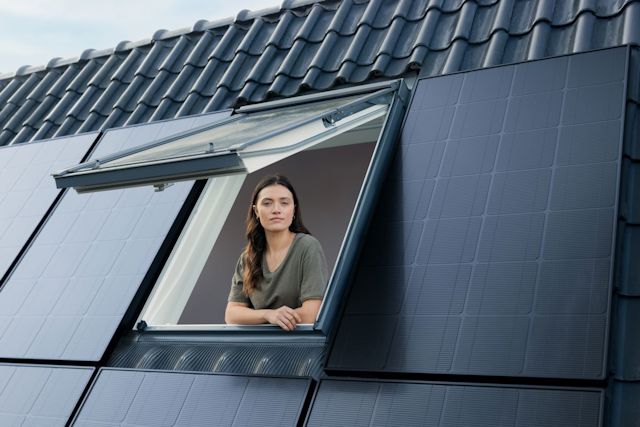 Vrouw kijkt uit dakraam, op het dak liggen zonnepanelen