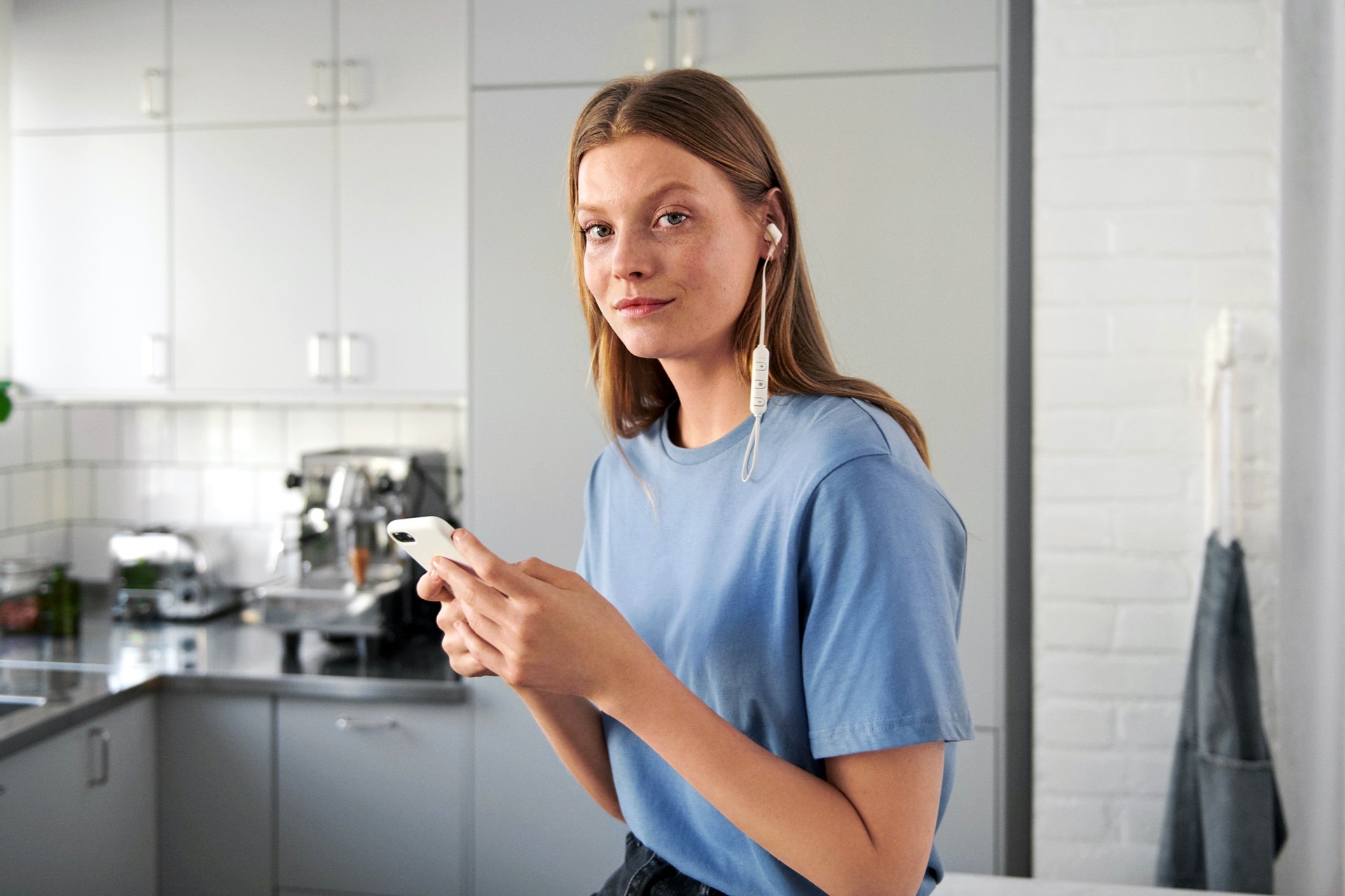 Jonge vrouw in keuken met oortjes in en in de hand mobieltje met Energie app