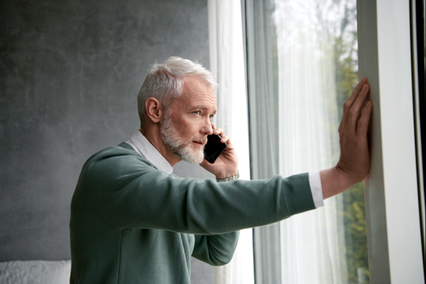 Man met groene trui geleund tegen het raam belt over hulp bij betaalproblemen
