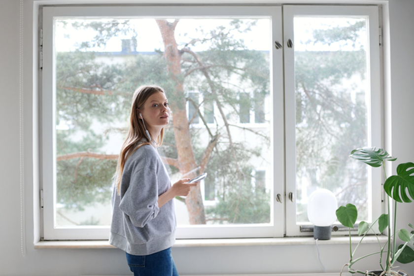 Jonge vrouw met mobiel en oortjes in voor het raam