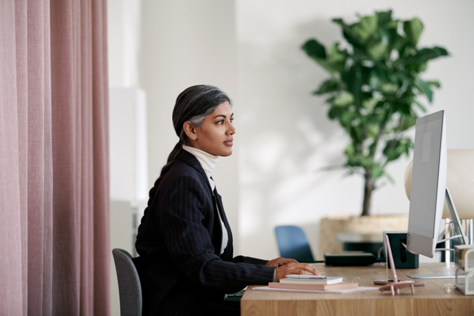 Office manager met donker jasje achter haar bureau - nieuwe opzegvergoeding