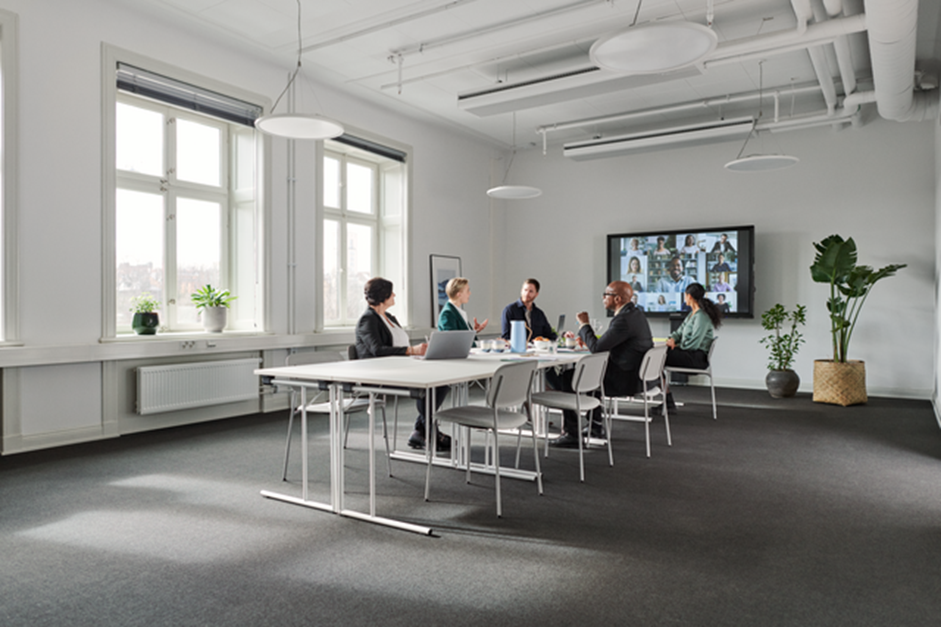 Collega's in hybride vergadering over termijnbedrag met 5 op kantoor aan een vergadertafel en de rest online op een groot scherm