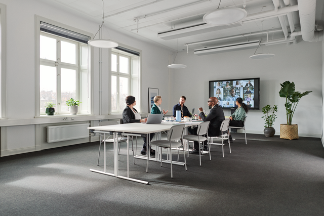 Hybride vergadering met 5 collega's aan vergadertafel en rest online op groot scherm