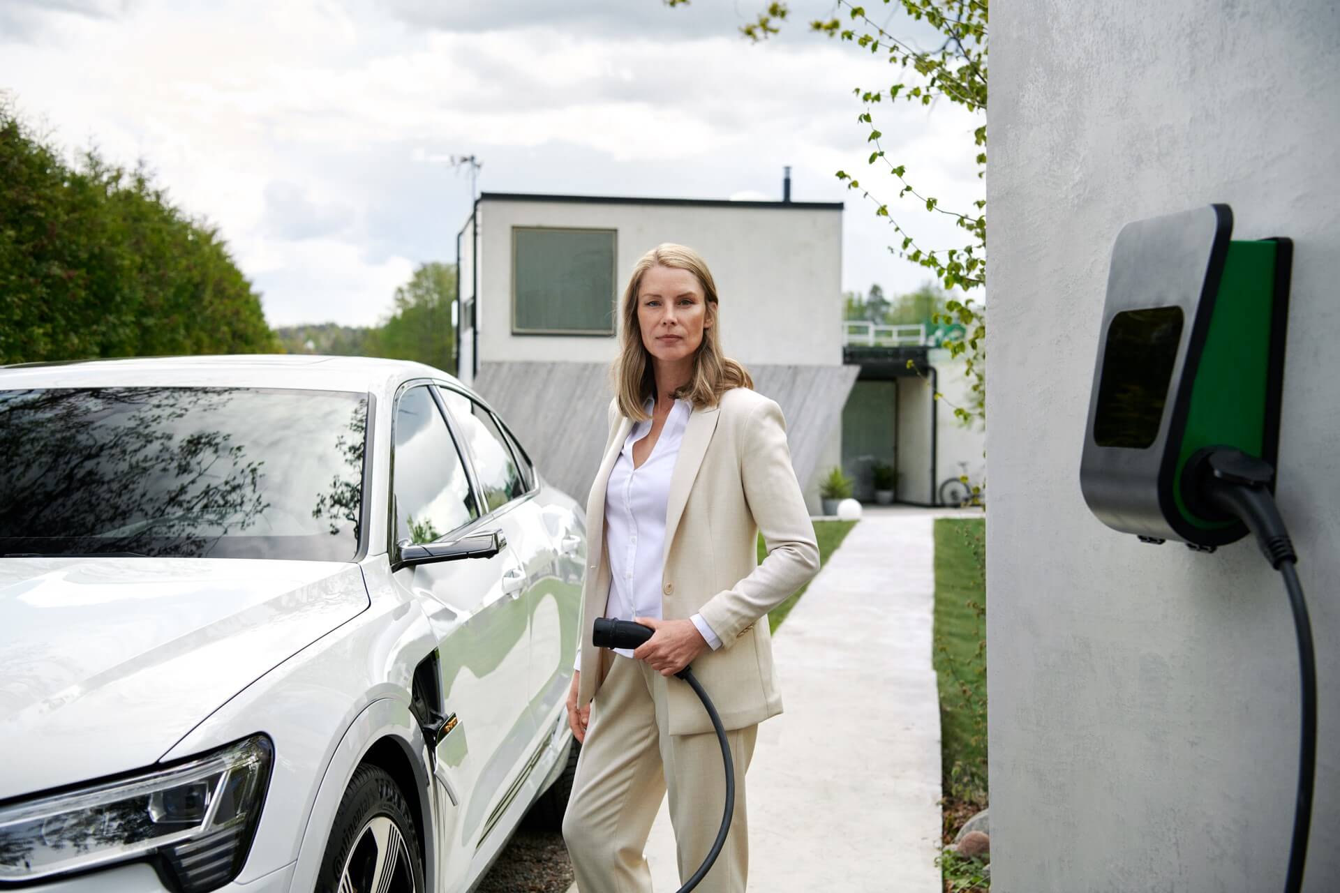 Vrouw in licht jasje bij witte auto aan oplader - Milieu Investeringsaftrek MIA