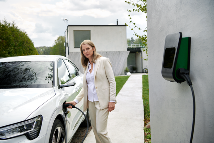 Vrouw laadt witte elektrische auto thuis op - ISDE: subsidie voor het verduurzamen van je bedrijfspand 