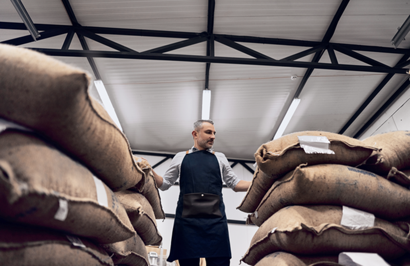 Een  man staat in een loods met zakken koffiebonen en denkt na over wat de energie veranderingen in 2024
