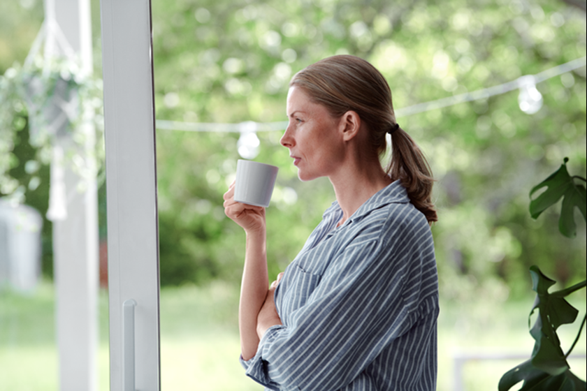 Vrouw drinkt thee en kijkt relaxt door het raam naar de tuin