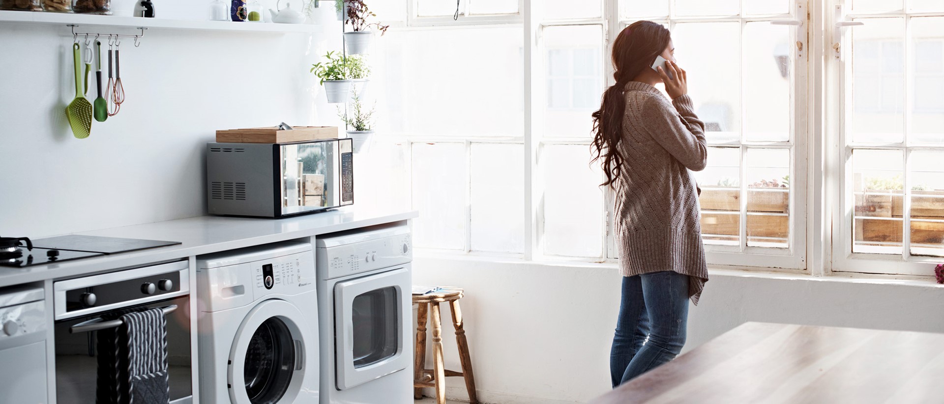 Vrouw staat te bellen naast de wasmachine | Vattenfall energie stroomverbruik berekenen